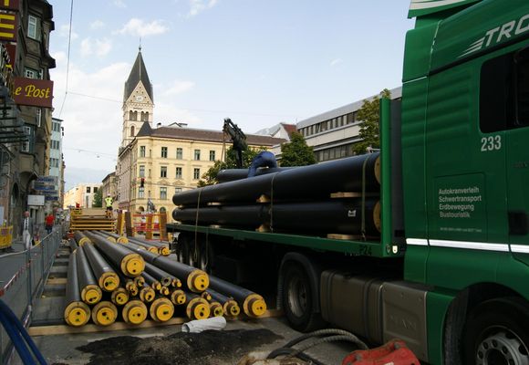 LKW mit Rohre als Beladung auf einer Straße vor einer Kirche